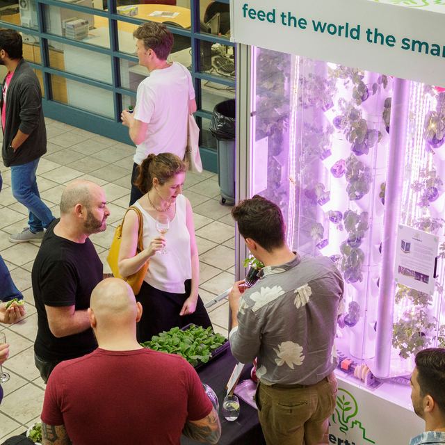 Visitors at an agtech startup stand with a vertical hydroponic growing wall