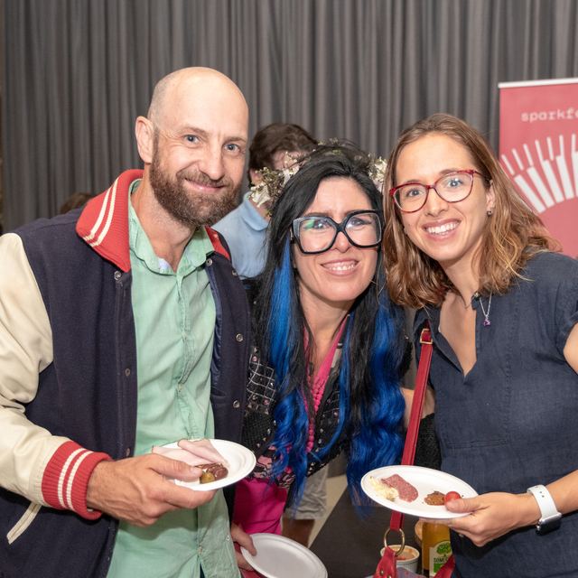 Three attendees with plates of food in front of a Spark Festival banner