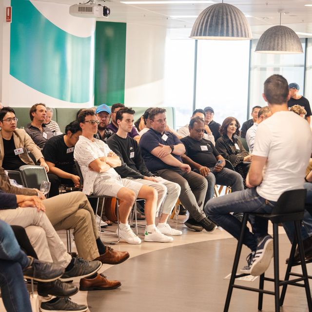 An audience on stools listening to a session in a bright open workspace
