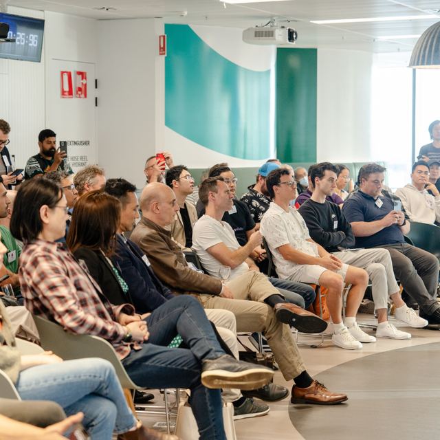 An audience seated in a bright room while the session is filmed from the back